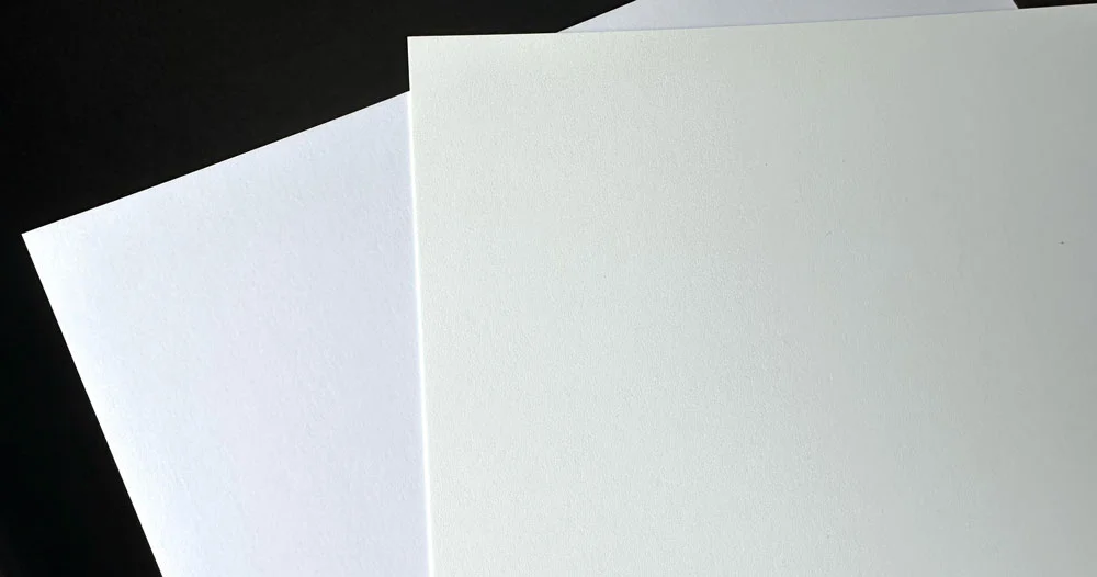 Two pieces of paper, one is bright white one is warm white